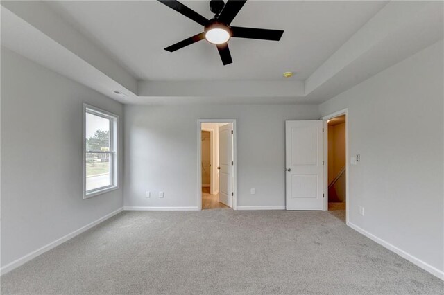 unfurnished bedroom featuring ceiling fan, a raised ceiling, and light carpet