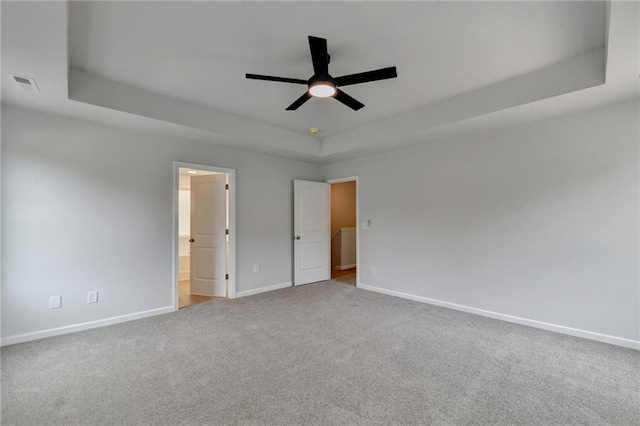 unfurnished bedroom with carpet flooring, ensuite bathroom, a tray ceiling, and ceiling fan