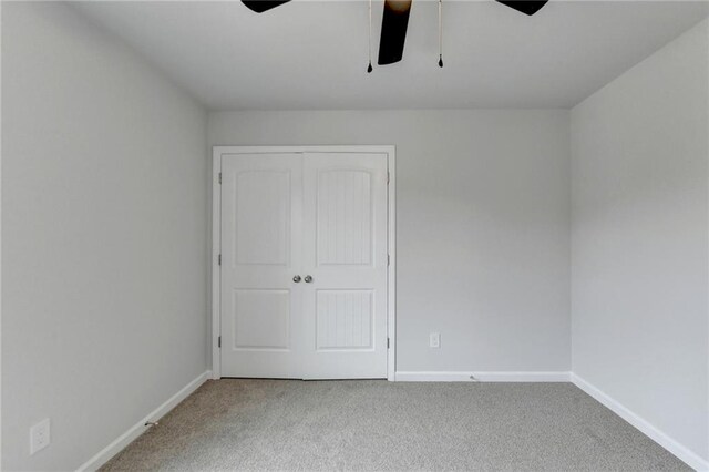 unfurnished bedroom with a closet, light colored carpet, and ceiling fan