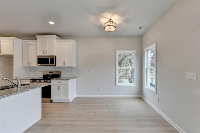 kitchen featuring appliances with stainless steel finishes, white cabinetry, light stone countertops, light hardwood / wood-style flooring, and sink