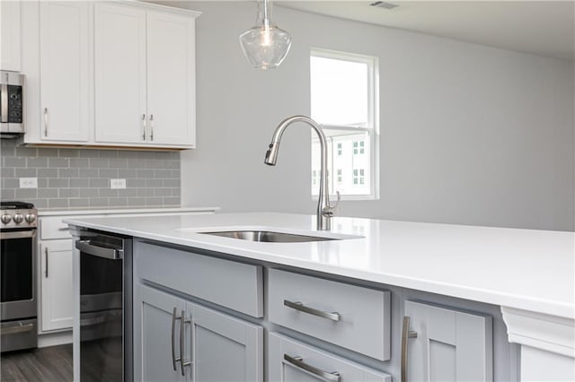 kitchen featuring appliances with stainless steel finishes, backsplash, sink, white cabinetry, and hanging light fixtures