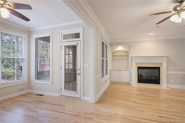 unfurnished living room with light wood-type flooring, a ceiling fan, a wealth of natural light, and ornamental molding