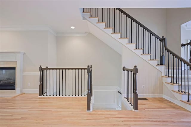 staircase with a fireplace, wood finished floors, baseboards, ornamental molding, and recessed lighting