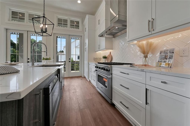 kitchen with wall chimney exhaust hood, white cabinetry, high end range, and french doors