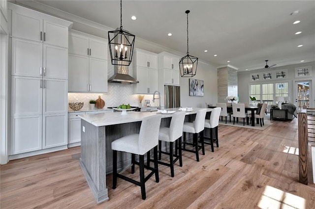 kitchen featuring decorative light fixtures, light hardwood / wood-style floors, a large island with sink, and white cabinetry