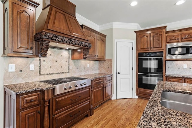 2602 Alcovy Club Dr, Dacula, GA 30019 - kitchen with appliances with stainless steel finishes, premium range hood, light wood finished floors, crown molding, and dark stone countertops