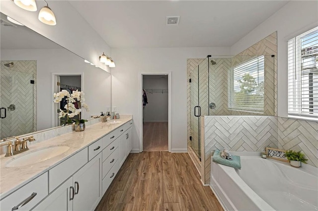 bathroom featuring a stall shower, wood finished floors, a walk in closet, and a bath