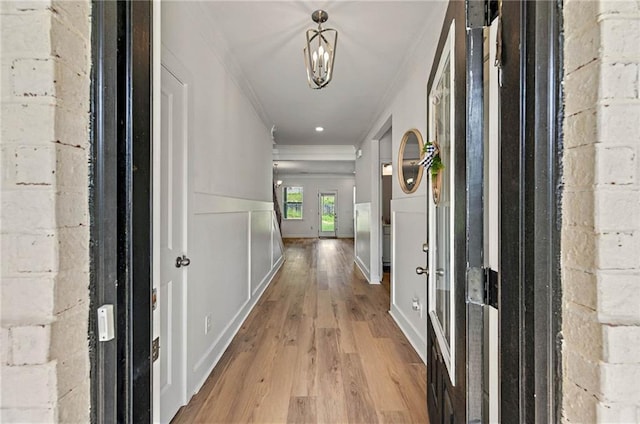 corridor with light wood-style flooring, ornamental molding, and baseboards