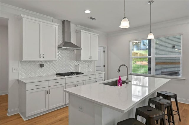 kitchen featuring a sink, wall chimney range hood, light wood-type flooring, decorative backsplash, and white cabinetry