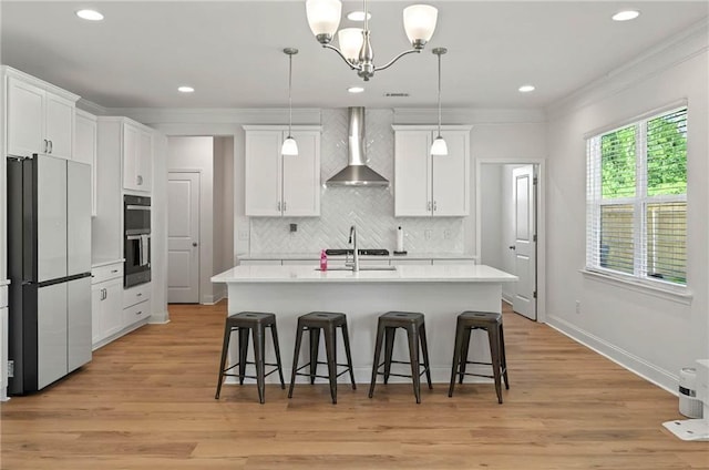 kitchen with wall chimney exhaust hood, freestanding refrigerator, light countertops, white cabinetry, and crown molding