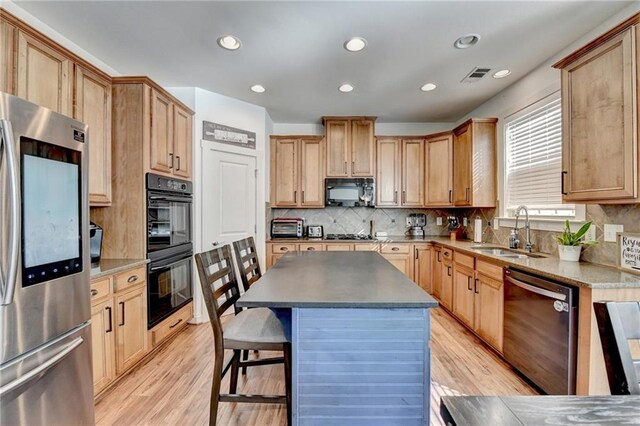 kitchen featuring backsplash, sink, black appliances, light hardwood / wood-style floors, and a kitchen island