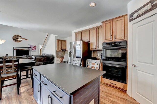 kitchen with double oven, stainless steel fridge, a center island, and light hardwood / wood-style floors