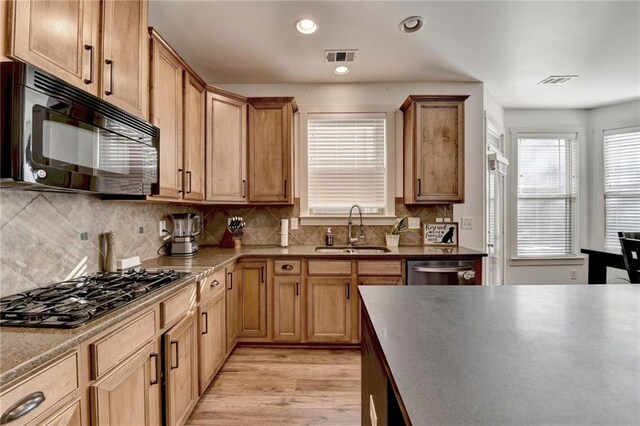 kitchen with appliances with stainless steel finishes, backsplash, light hardwood / wood-style floors, and sink