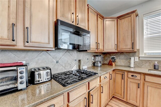 kitchen featuring light stone countertops, backsplash, light hardwood / wood-style floors, and black appliances