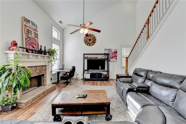 living room with a high ceiling, hardwood / wood-style flooring, a brick fireplace, and ceiling fan