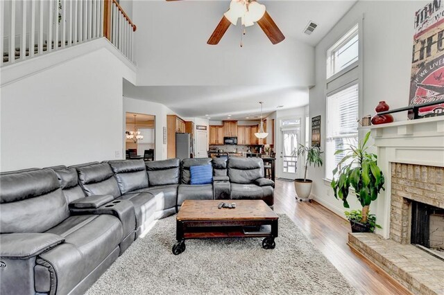 living room featuring a fireplace, a high ceiling, ceiling fan with notable chandelier, and light hardwood / wood-style flooring