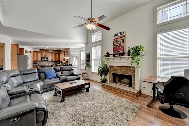 living room with a high ceiling, light hardwood / wood-style floors, a brick fireplace, and ceiling fan