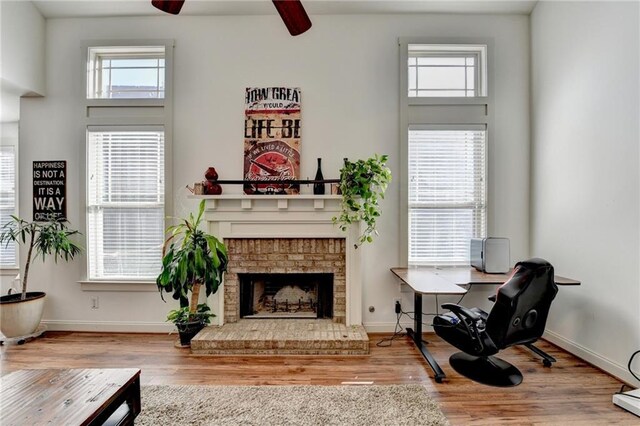 living area featuring ceiling fan, wood-type flooring, and a fireplace