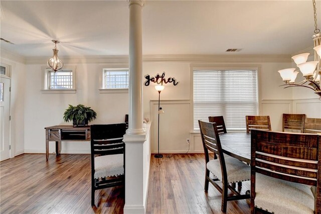 dining area featuring an inviting chandelier, hardwood / wood-style flooring, ornate columns, and crown molding