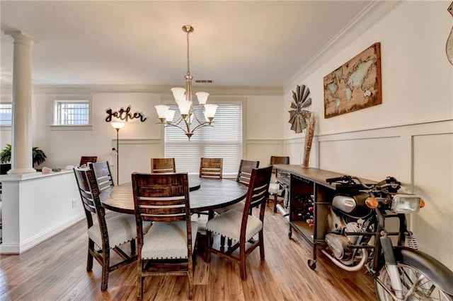 dining room with wood-type flooring, ornate columns, ornamental molding, and a notable chandelier