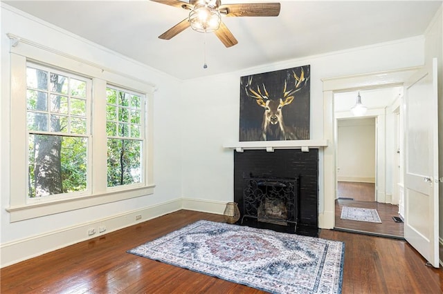 living area featuring baseboards, wood-type flooring, a ceiling fan, and a fireplace