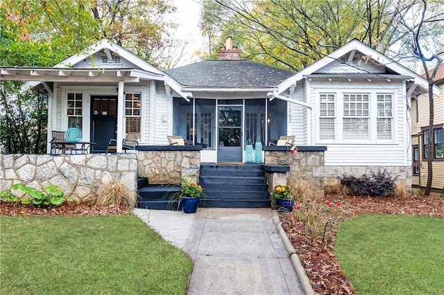 view of front of property with stone siding, covered porch, a front yard, a sunroom, and a chimney