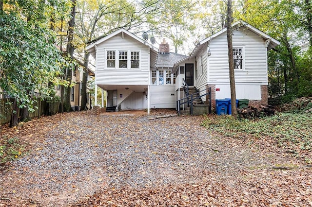 rear view of property featuring a carport, stairway, driveway, and a chimney