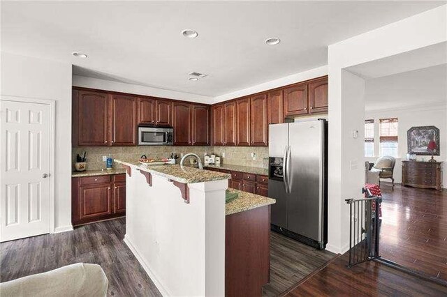 316 Branch Valley Dr NE, Dallas, GA 30132 - kitchen featuring appliances with stainless steel finishes, light stone counters, dark wood finished floors, tasteful backsplash, and a kitchen island with sink