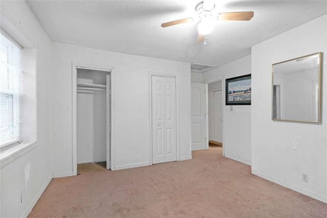 unfurnished bedroom featuring light colored carpet, ceiling fan, and multiple closets