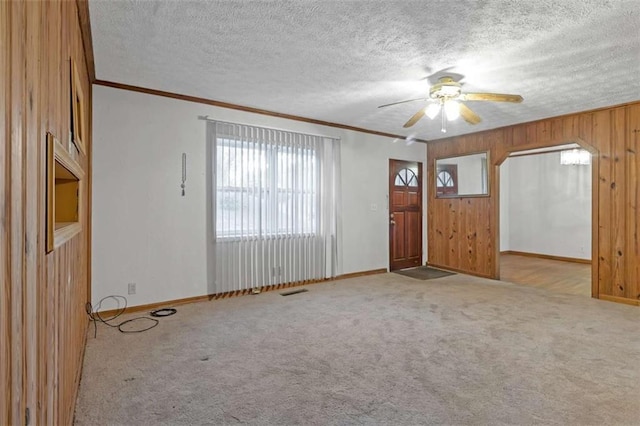 entryway with ceiling fan, crown molding, light colored carpet, a textured ceiling, and wooden walls