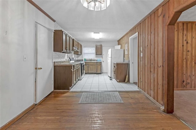 kitchen featuring crown molding, sink, electric range, white refrigerator, and wood walls