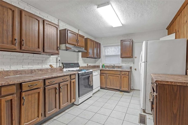 kitchen featuring a textured ceiling, light tile patterned flooring, white appliances, and sink