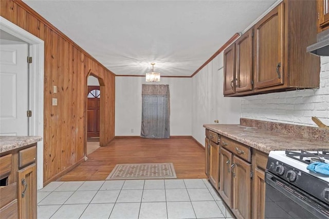 kitchen with pendant lighting, black gas range, crown molding, light tile patterned floors, and extractor fan