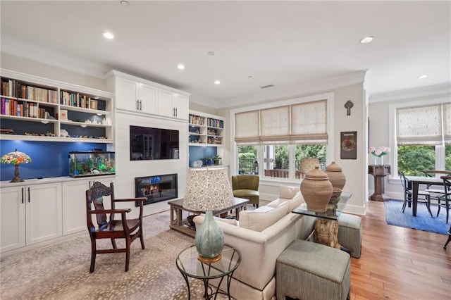 living room with light hardwood / wood-style floors, built in shelves, ornamental molding, and a large fireplace