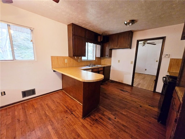 kitchen with kitchen peninsula, dark brown cabinets, sink, black / electric stove, and light wood-type flooring