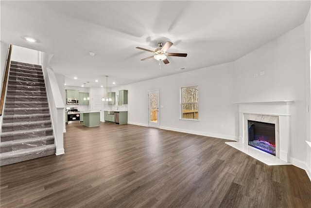 unfurnished living room with dark wood finished floors, stairway, ceiling fan, and a high end fireplace