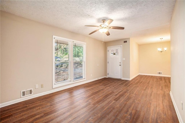 empty room with dark hardwood / wood-style flooring, ceiling fan with notable chandelier, and a textured ceiling