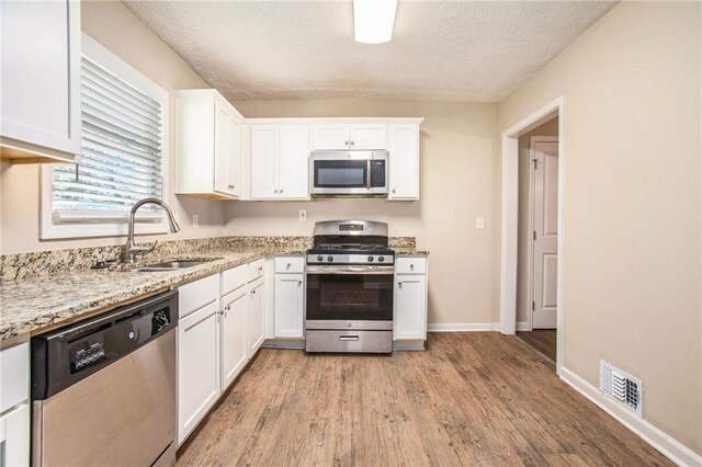 kitchen with light stone countertops, stainless steel appliances, sink, light hardwood / wood-style floors, and white cabinetry