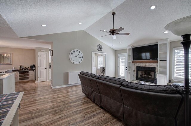 living room featuring lofted ceiling, dark wood-type flooring, ceiling fan, a textured ceiling, and a fireplace