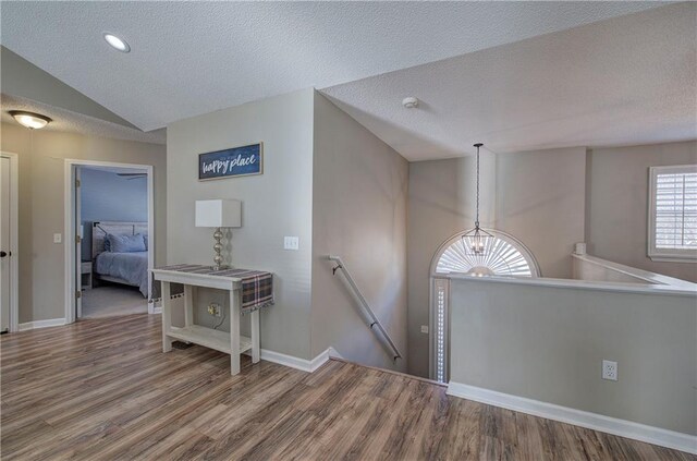 corridor featuring hardwood / wood-style floors, a textured ceiling, lofted ceiling, and a notable chandelier