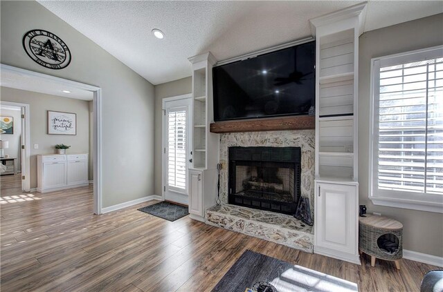 living room featuring a textured ceiling, vaulted ceiling, a stone fireplace, and wood-type flooring