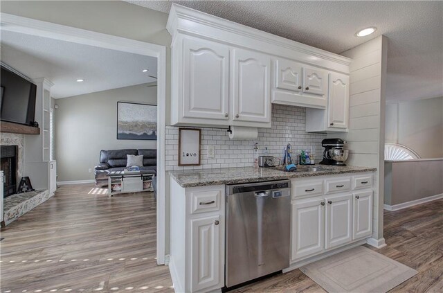 kitchen featuring a fireplace, vaulted ceiling, light hardwood / wood-style flooring, dishwasher, and white cabinetry