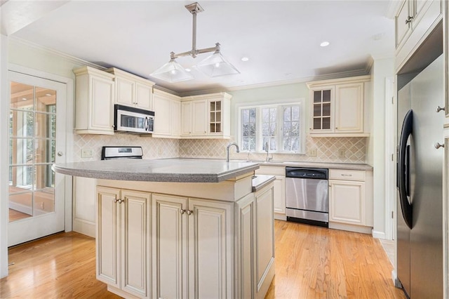 kitchen with cream cabinetry, appliances with stainless steel finishes, a kitchen island, and glass insert cabinets