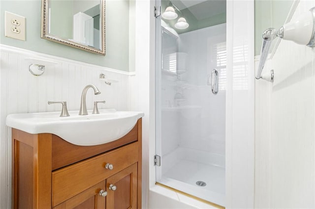 full bath featuring a stall shower, a wainscoted wall, and vanity