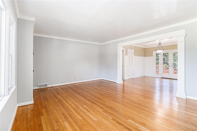 empty room featuring light wood finished floors, visible vents, ornamental molding, french doors, and ornate columns