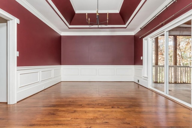 spare room with hardwood / wood-style floors, a notable chandelier, a raised ceiling, and crown molding