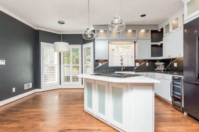 kitchen with pendant lighting, a center island, decorative backsplash, white cabinetry, and beverage cooler