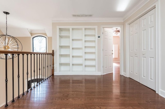 corridor featuring a chandelier, built in shelves, dark hardwood / wood-style flooring, and crown molding