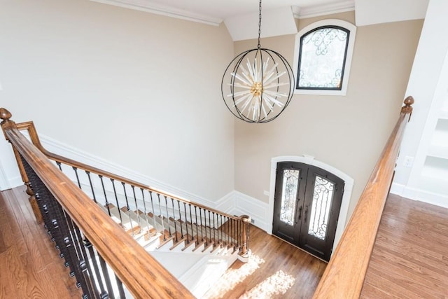 entrance foyer featuring hardwood / wood-style floors, a notable chandelier, ornamental molding, and french doors