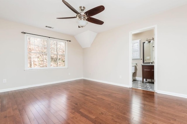 interior space with vaulted ceiling, dark hardwood / wood-style floors, ensuite bath, and ceiling fan